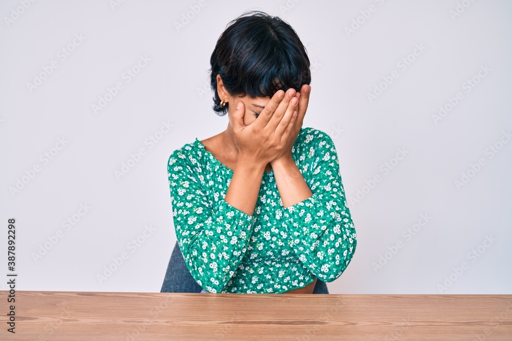 Beautiful brunettte woman wearing casual clothes sitting on the table with sad expression covering face with hands while crying. depression concept. Beautiful brunettte woman wearing casual clothes sitting on the table with sad expression covering face with hands while crying. depression concept.