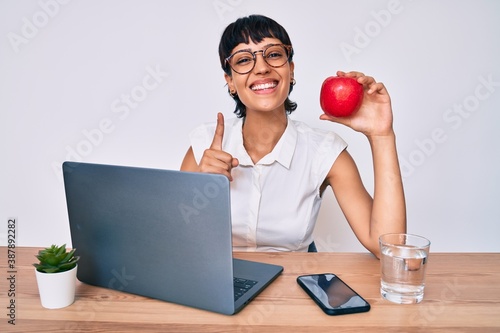 Photos Beautiful brunettte woman working at the office eating healthy apple surprised w