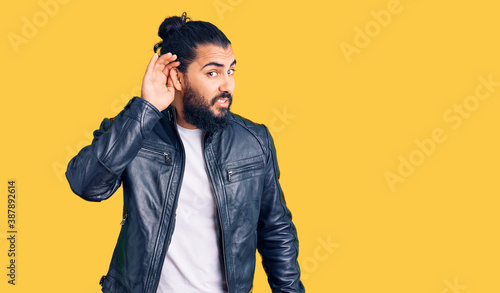 Young arab man wearing casual leather jacket smiling with hand over ear listening an hearing to rumor or gossip. deafness concept. © Krakenimages.com