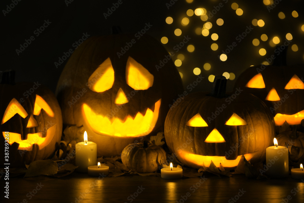 Fototapeta premium Pumpkin jack o'lanterns, autumn leaves and candles on table against blurred background. Halloween decor