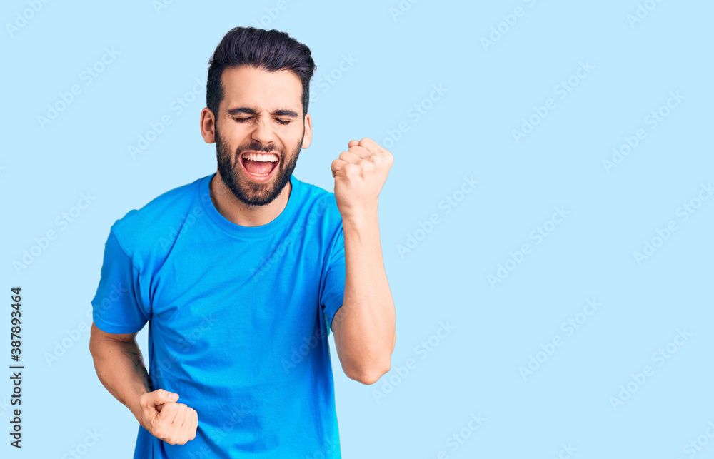 Young handsome man with beard wearing casual t-shirt celebrating surprised and amazed for success with arms raised and eyes closed. winner concept. Young handsome man with beard wearing casual t-shirt celebrating surprised and amazed for success with arms raised and eyes closed. winner concept.
