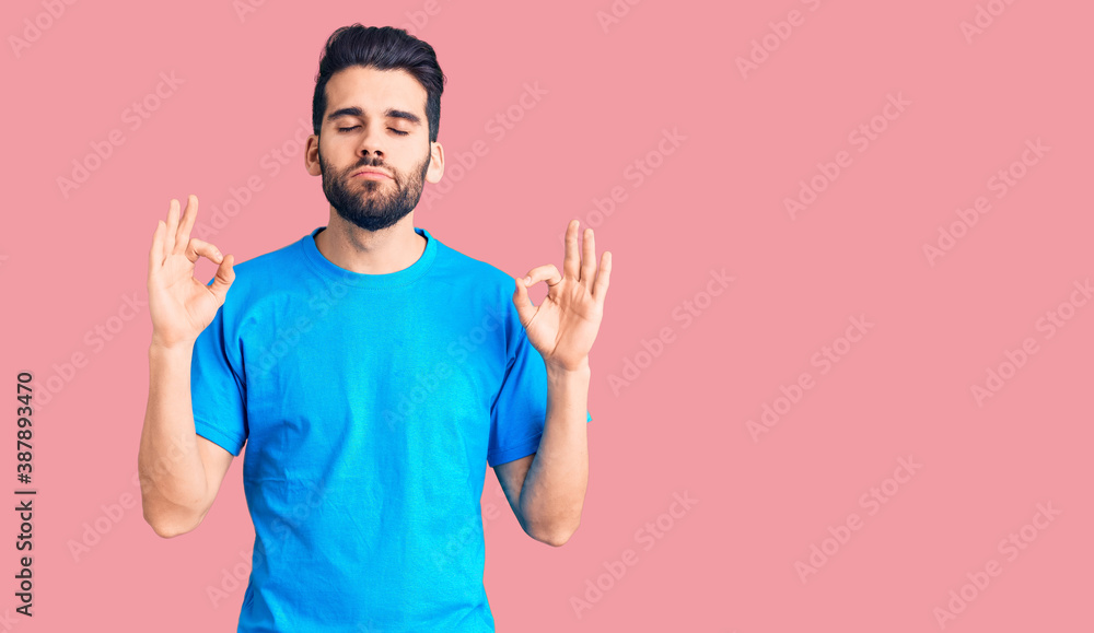 Fototapeta premium Young handsome man with beard wearing casual t-shirt relaxed and smiling with eyes closed doing meditation gesture with fingers. yoga concept.