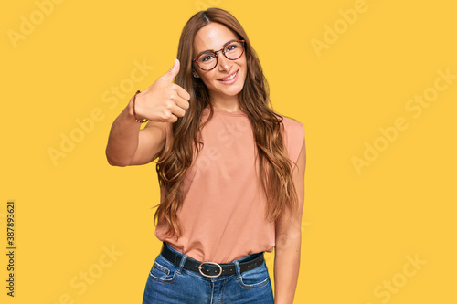 Young hispanic woman wearing casual clothes and glasses doing happy thumbs up gesture with hand. approving expression looking at the camera showing success.