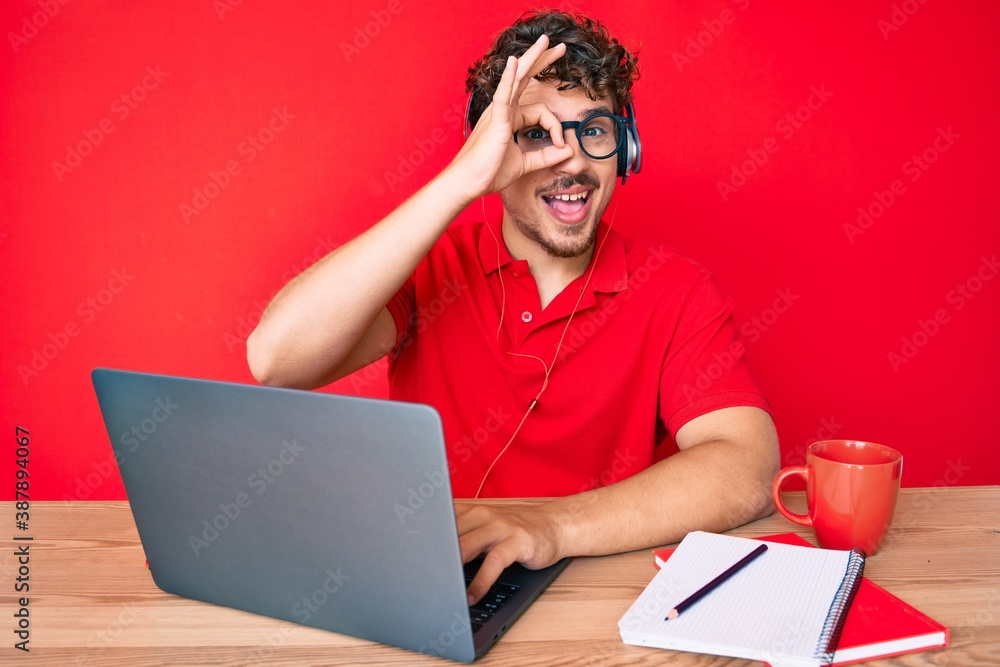 Young caucasian man with curly hair working at the office drinking a cup of coffee smiling happy doing ok sign with hand on eye looking through fingers Young caucasian man with curly hair working at the office drinking a cup of coffee smiling happy doing ok sign with hand on eye looking through fingers