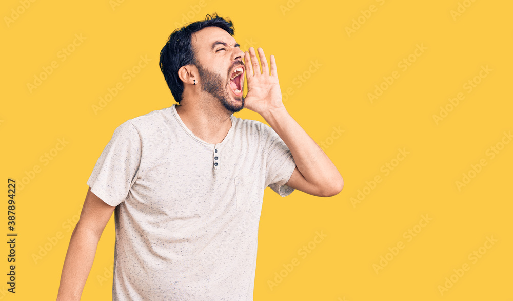 Young hispanic man wearing casual clothes shouting and screaming loud to side with hand on mouth. communication concept. Young hispanic man wearing casual clothes shouting and screaming loud to side with hand on mouth. communication concept.