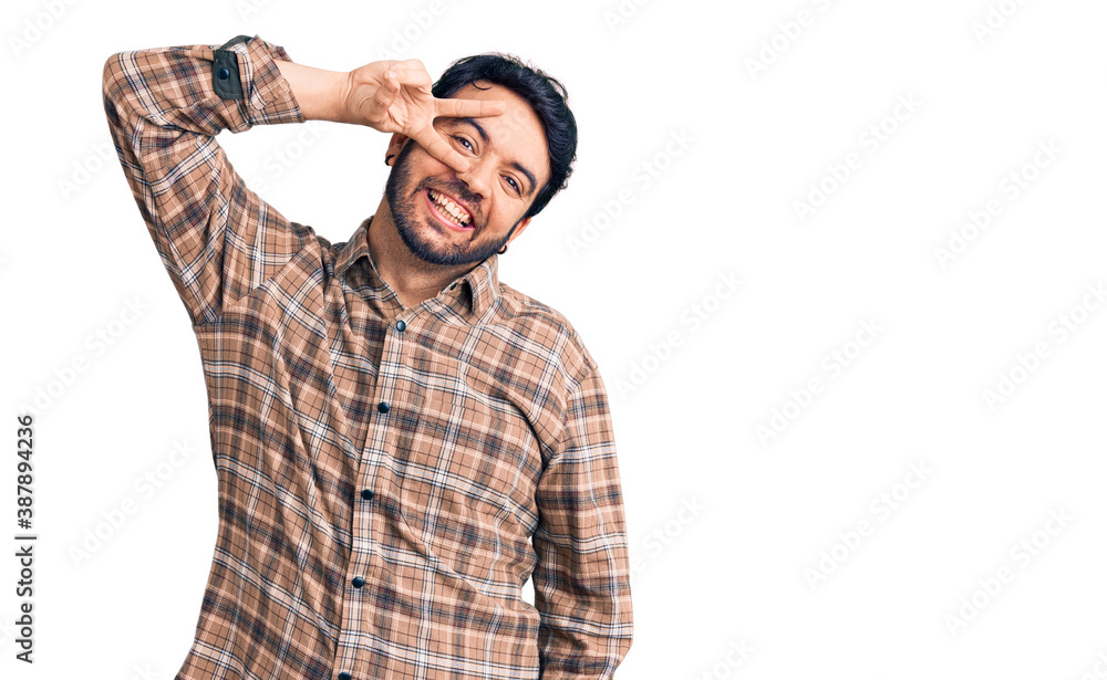 Young hispanic man wearing casual clothes doing peace symbol with fingers over face, smiling cheerful showing victory Young hispanic man wearing casual clothes doing peace symbol with fingers over face, smiling cheerful showing victory