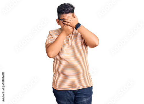 Little boy kid wearing casual clothes and glasses covering eyes and mouth with hands, surprised and shocked. hiding emotion