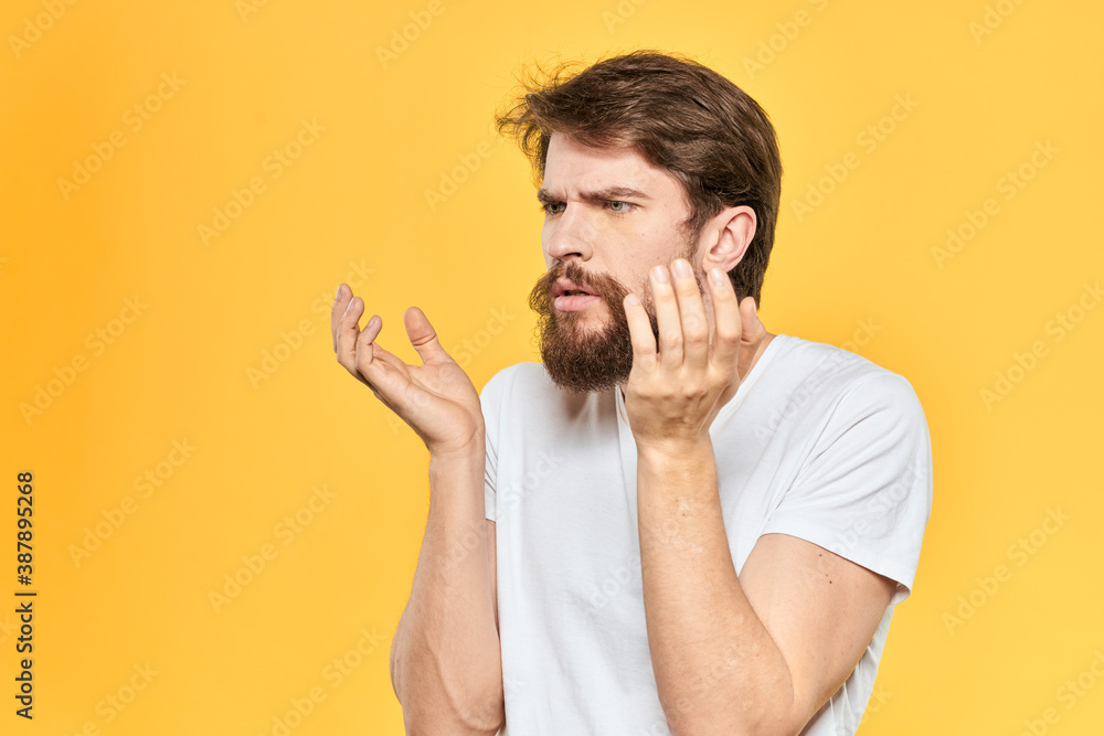 Bearded man in a white T-shirt gestures with his hands emotions studio yellow background Bearded man in a white T-shirt gestures with his hands emotions studio yellow background