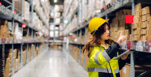 Portrait of smiling asian engineer in helmets woman order details on tablet computer for checking goods and supplies on shelves with goods background in warehouse.logistic and business export