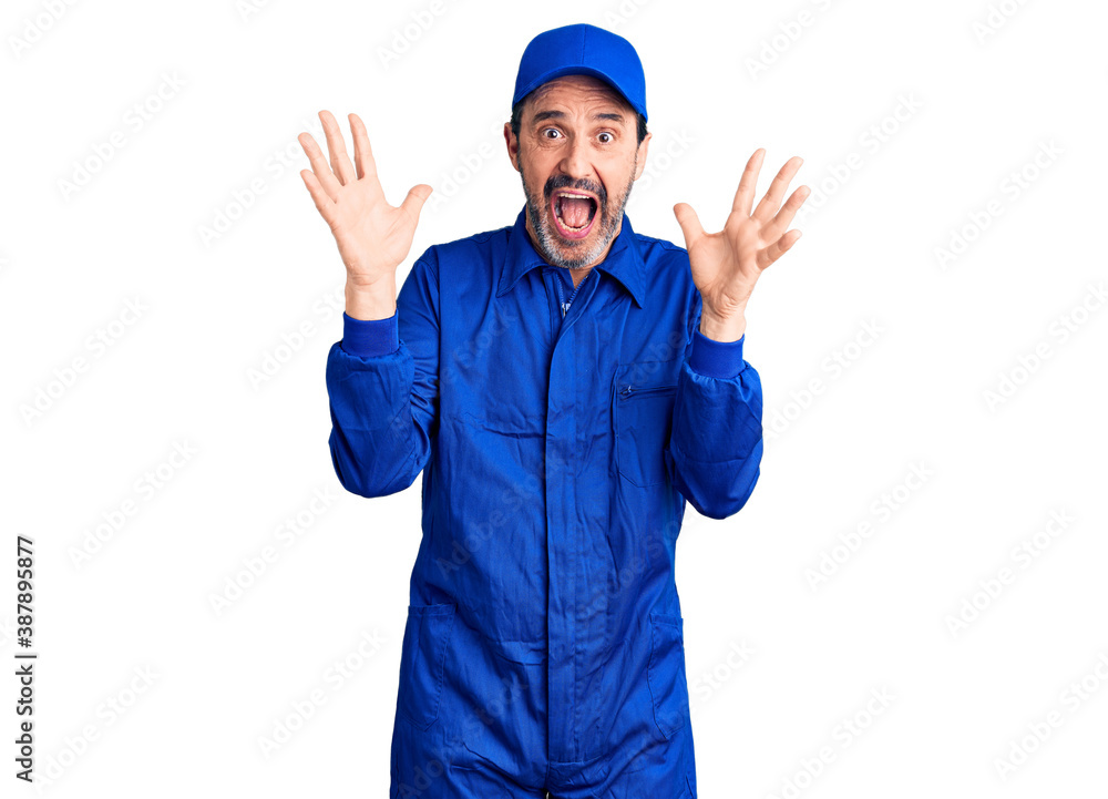 Middle age handsome man wearing mechanic uniform celebrating crazy and amazed for success with arms raised and open eyes screaming excited. winner concept