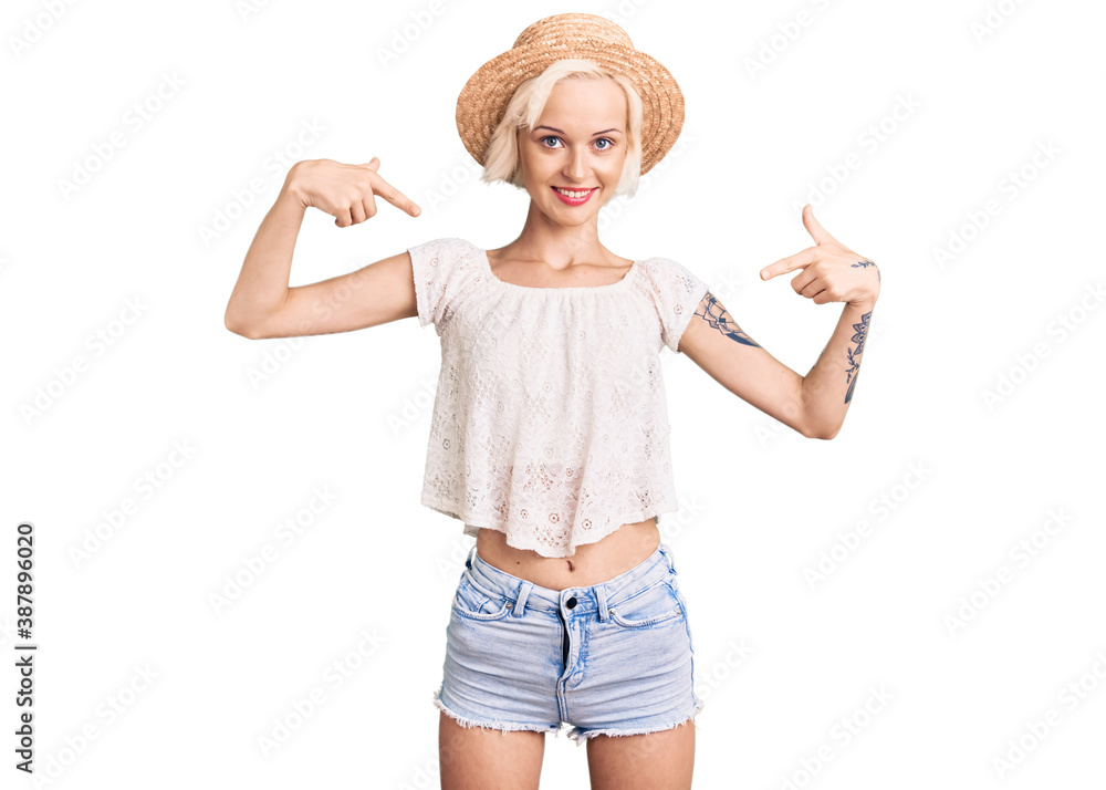 Young blonde woman with tattoo wearing summer hat looking confident with smile on face, pointing oneself with fingers proud and happy. Young blonde woman with tattoo wearing summer hat looking confident with smile on face, pointing oneself with fingers proud and happy.