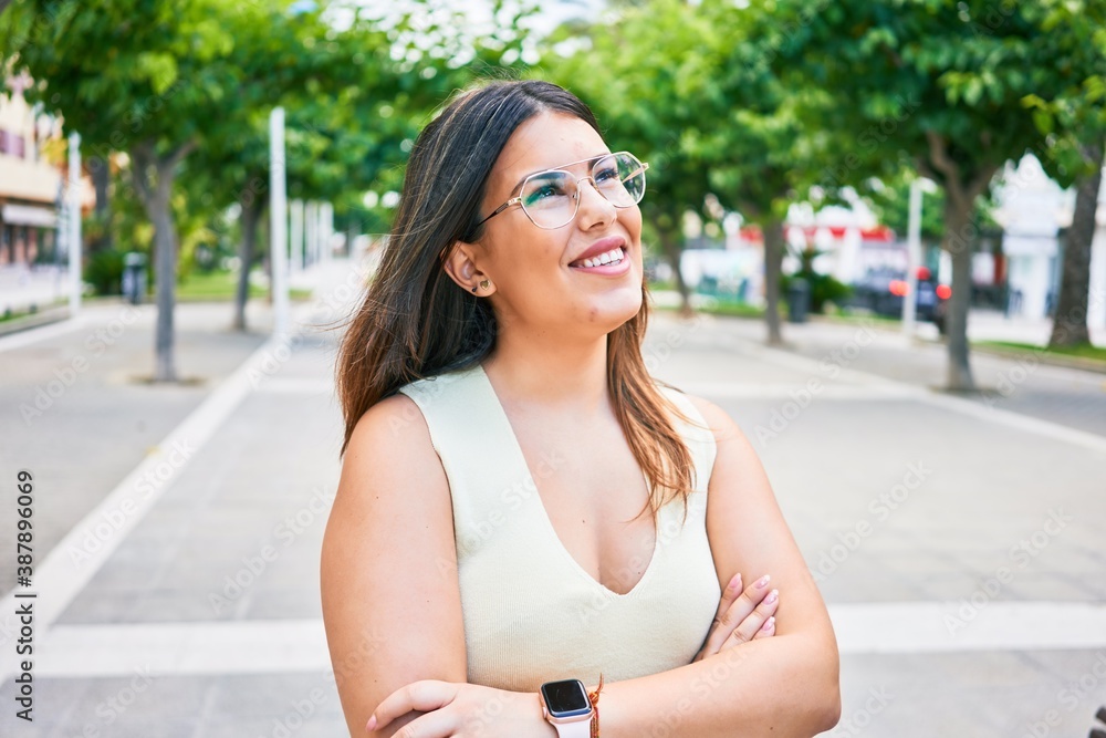 Young beautiful woman smiling happy with arms crossed. Standing with smile on face looking to the side walking at town street. Young beautiful woman smiling happy with arms crossed. Standing with smile on face looking to the side walking at town street.