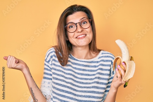 Beautiful caucasian woman eating banana as healthy snack screaming proud, celebrating victory and success very excited with raised arm