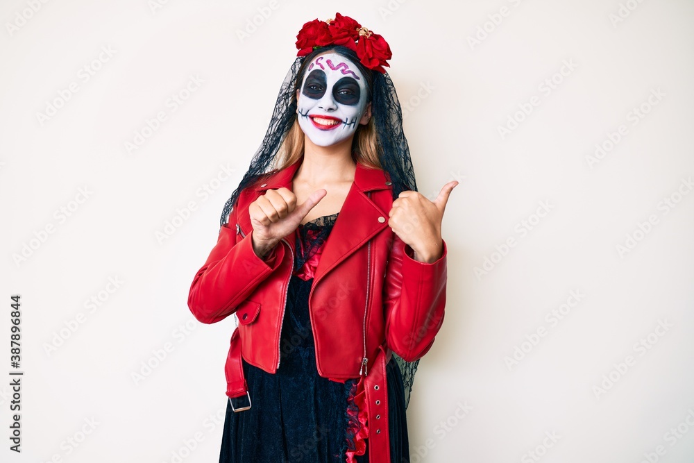 Woman wearing day of the dead costume over white pointing to the back behind with hand and thumbs up, smiling confident Woman wearing day of the dead costume over white pointing to the back behind with hand and thumbs up, smiling confident