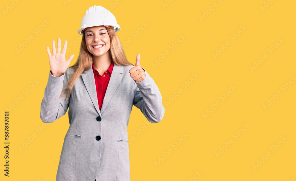 Beautiful young woman wearing architect hardhat showing and pointing up with fingers number six while smiling confident and happy.