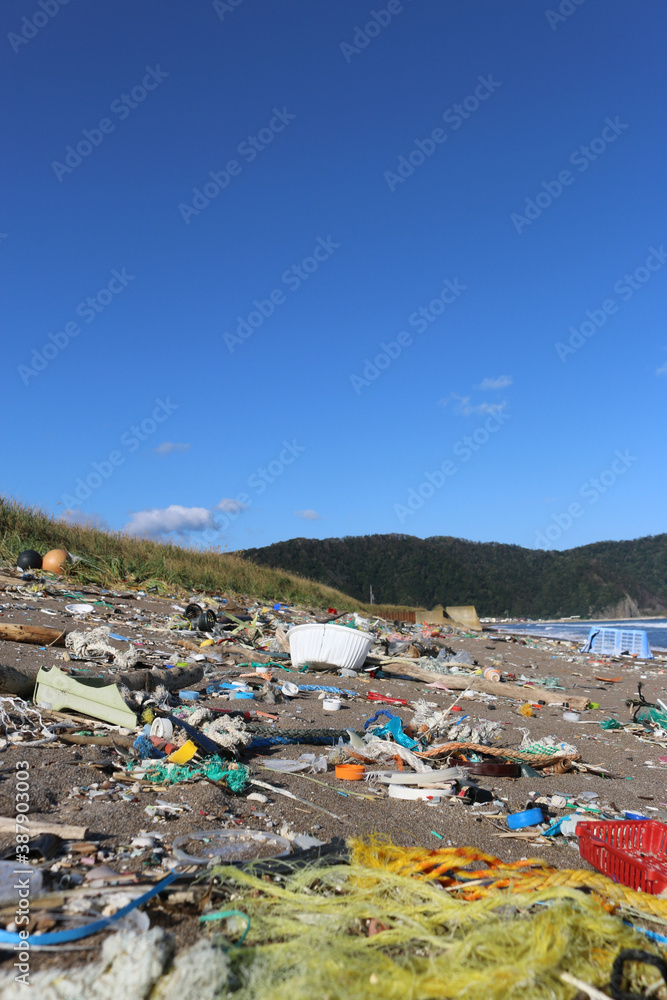 Sandy beach environment covered in colourful plastic waste rubbish on sunny day