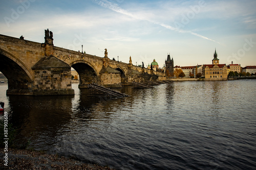 view of the old stone bridge from the 14th century in the center of the city of prague on the flowing river Vltava river there are statues and the sky is blue at sunset in the Czech Republic