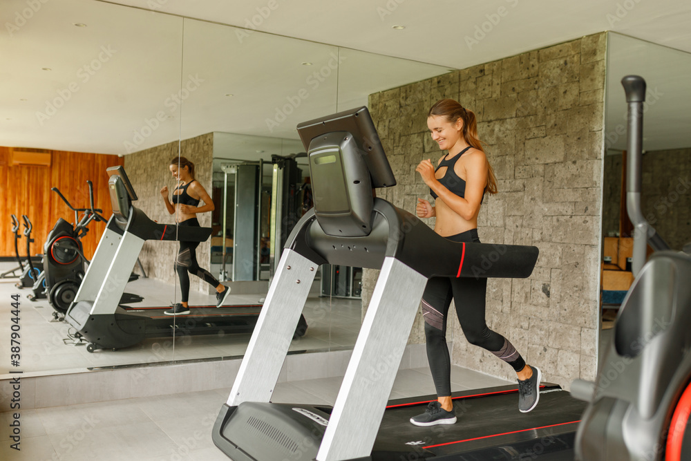 Happy smiling young sports woman is working out in gym. Doing cardio training on treadmill, running Happy smiling young sports woman is working out in gym. Doing cardio training on treadmill, running
