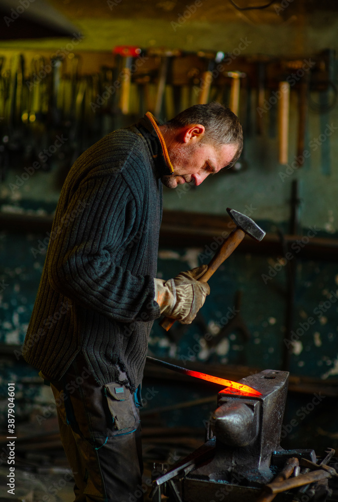 A blacksmith forging a red-hot iron billet on an anvil with a hammer. Handicraft concept A blacksmith forging a red-hot iron billet on an anvil with a hammer. Handicraft concept