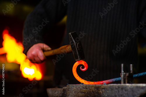 A blacksmith forging a curl from a red-hot flattened billet with a hammer. Handmade in the forge concept