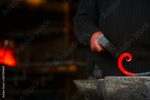 Fotografija A close-up image of a blacksmith's hands forging a spiral from a red-hot billet against the background of a forge