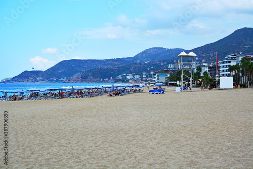 Fototapeta Naklejka Na Ścianę i Meble -  Coast of the Mediterranean sea, Turkey, Alanya. Wide city sandy Cleopatra beach with sun umbrellas and sun beds with people. Recreation, swimming, sunbathing at the resort