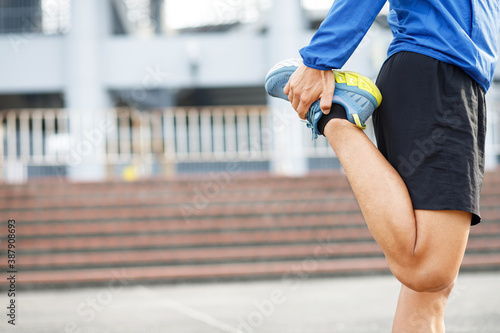 young man runner stretching for warming up before running or working out on the road. Track and Field Athlete exercise. Fitness and sport healthy lifestyle concept. copy space banner.