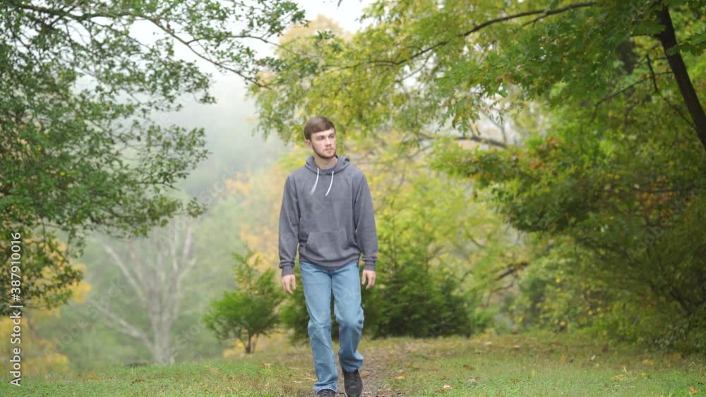 A caucasian man in a hoodie walks toward the camera in a forest A caucasian man in a hoodie walks toward the camera in a forest