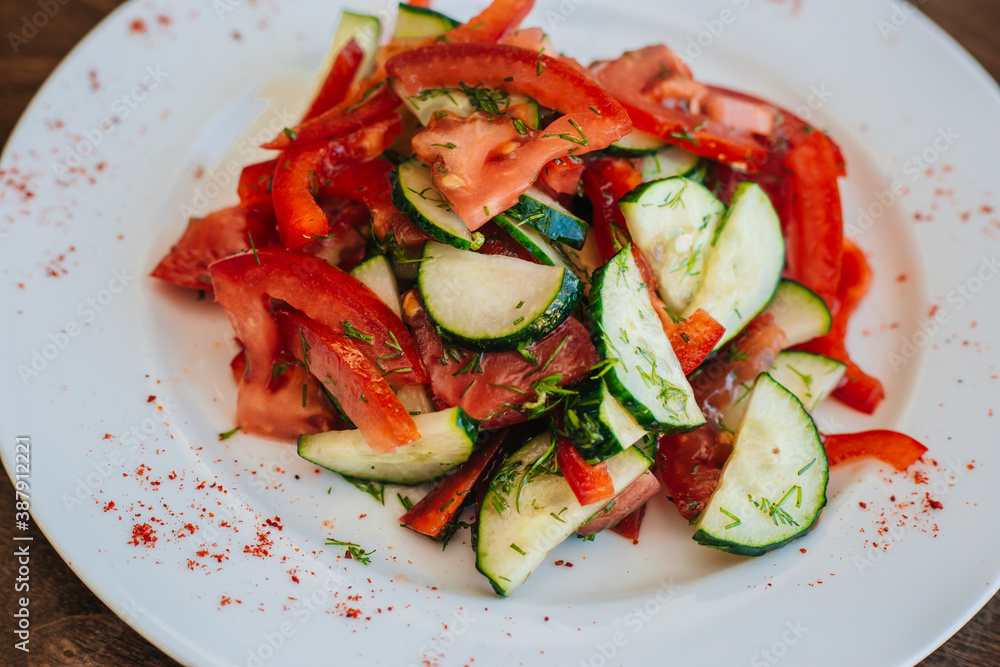 Classic salad with cucumbers and tomatoes sprinkled with dill. Diet food. On a white plate. Dish on a dark background. Classic salad with cucumbers and tomatoes sprinkled with dill. Diet food. On a white plate. Dish on a dark background.