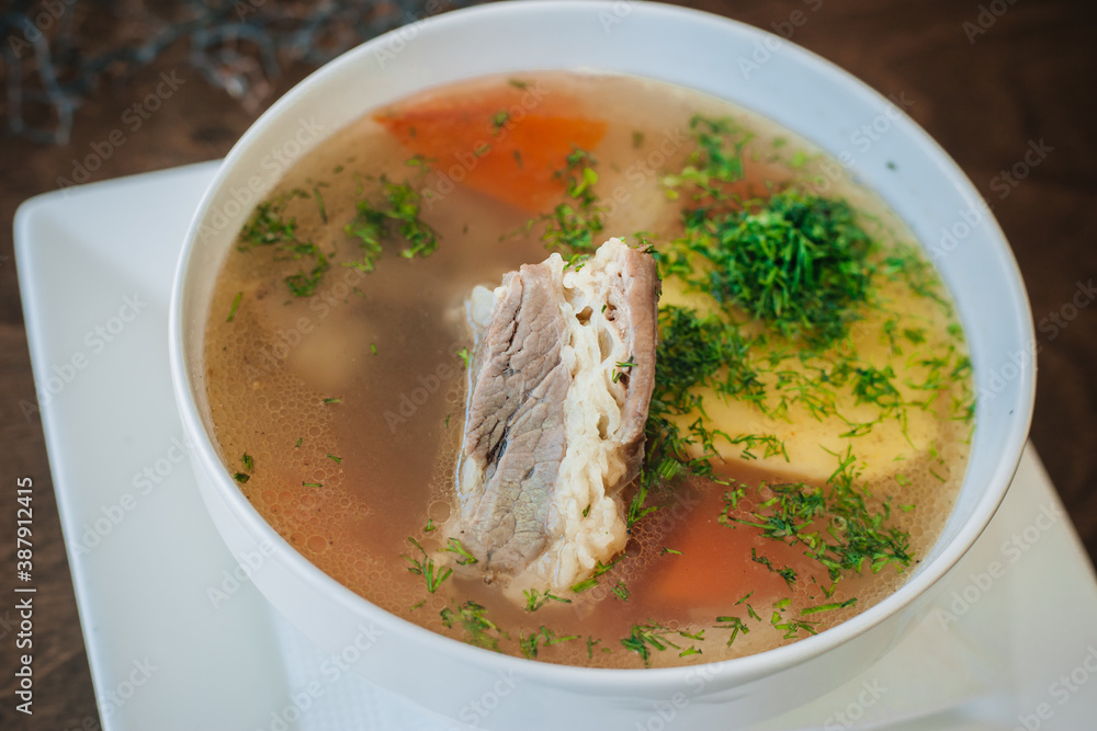 Diet soup with a small piece of pork and potatoes. Lean broth. Nutrition for gastritis. White bowl on a dark background Diet soup with a small piece of pork and potatoes. Lean broth. Nutrition for gastritis. White bowl on a dark background