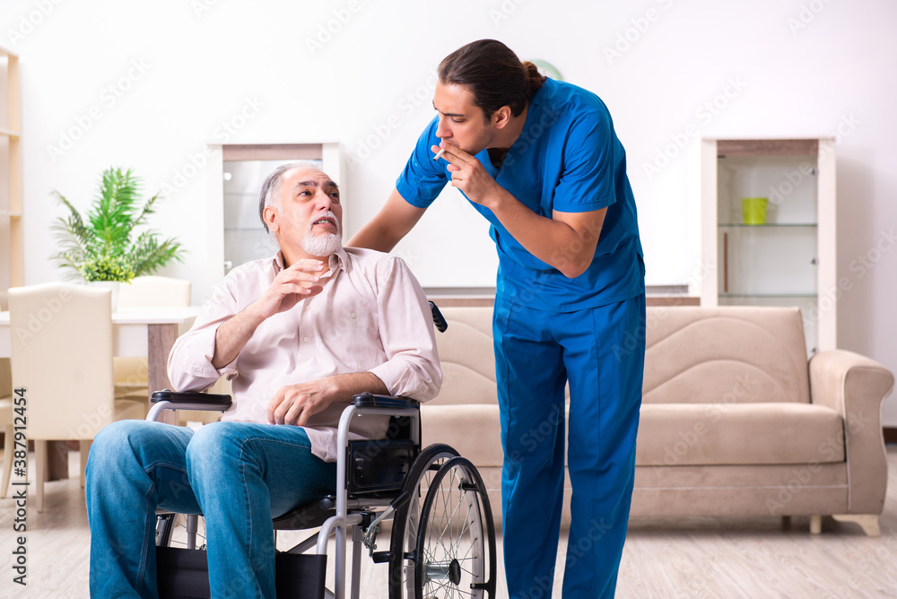 Old man in wheel-chair and young bad caregiver indoors Old man in wheel-chair and young bad caregiver indoors
