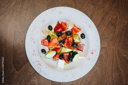 Diet salad. Tomatoes with cucumbers and olives, cubes of white soap and a cabbage leaf. Healthy food, white dish on a dark background
