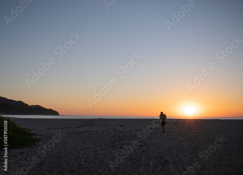 man walking in the sunset on a beautiful beach with a blue sky