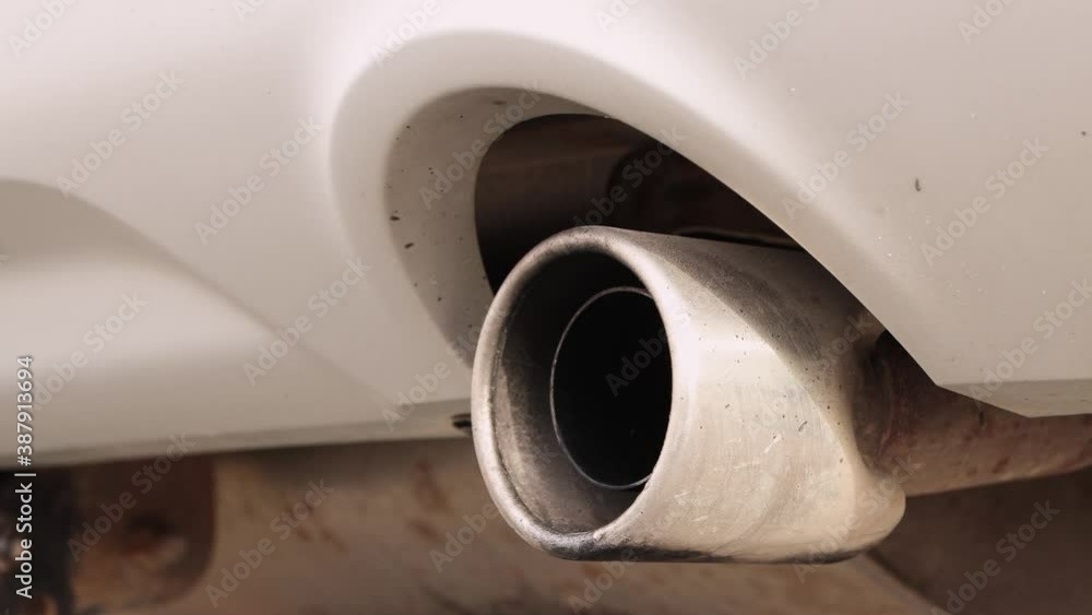 Closeup of the exhaust pipe of a working white car. The round pipe shakes slightly. Vehicle