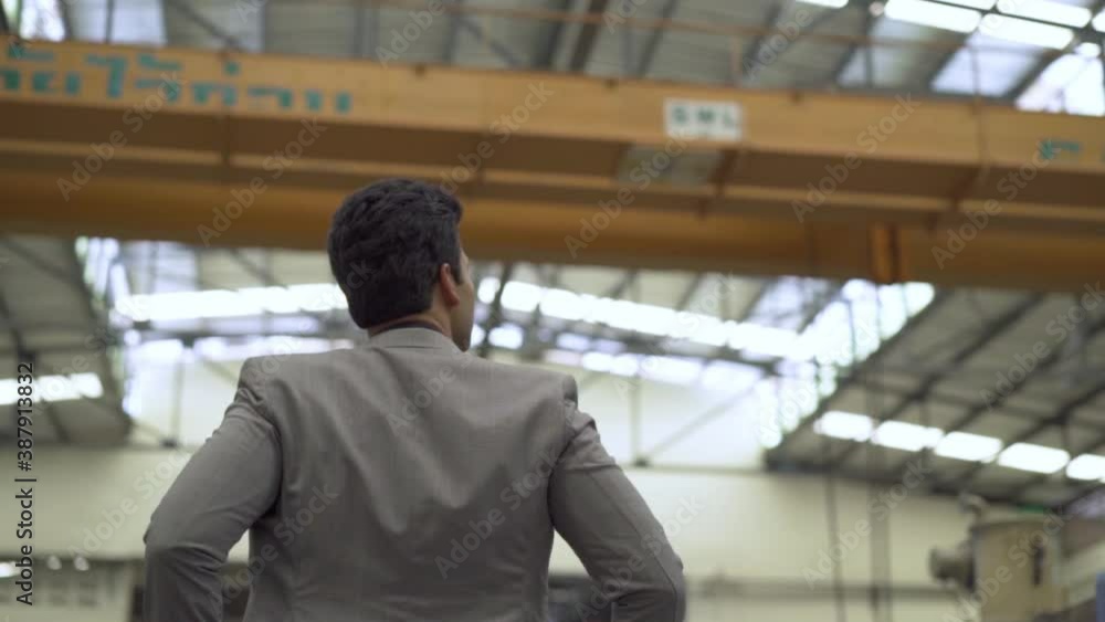 Young 20s Indian Asian factory business owner in formal suit walking inspecting. Ambitious businessman portrait in industrial background - Back Rear View - HD Slow Motion Footage Young 20s Indian Asian factory business owner in formal suit walking inspecting. Ambitious businessman portrait in industrial background - Back Rear View - HD Slow Motion Footage