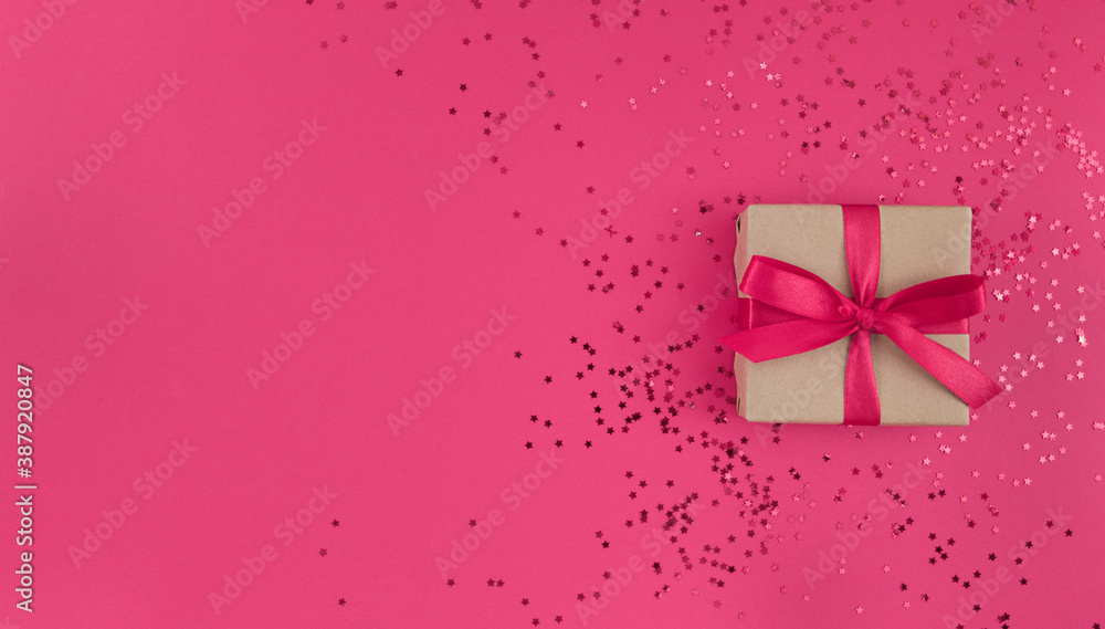 Gift box wrapped in a craft paper with pink ribbon with bow and confetti on pink background. Monochrome festive flat lay with copy space. Gift box wrapped in a craft paper with pink ribbon with bow and confetti on pink background. Monochrome festive flat lay with copy space.