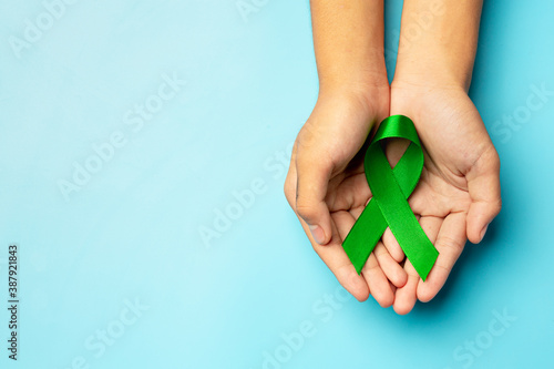 World Mental Health Day; green ribbon put in human's hands on blue background