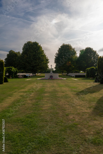 An open field leads up to a cross-topped monument commemorating the British lives lost during World War 2 at the Bayeux War Cemetery in Normandy, France. photo