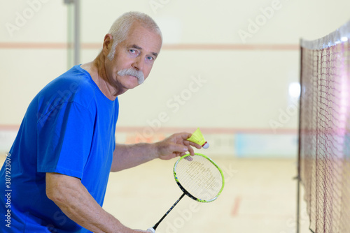 senior man playing badminton on indoor court
