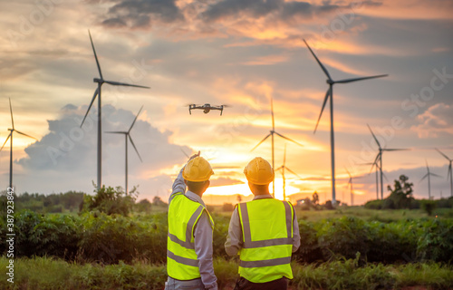 Fotografia two asian engineers male flying drone surveying and checking wind turbines from the high angle view of the field during beautiful sunset