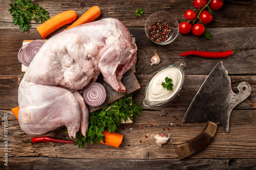 Raw fresh whole rabbit cut and meat cleaver, with ingredients for stewing sour cream, carrots, parsley, vegetables and garlic on a rustic table, top view