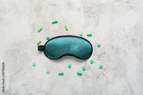 Sleeping mask and pills on light background