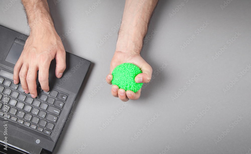Obraz premium Man squeezing stress ball while working with laptop.