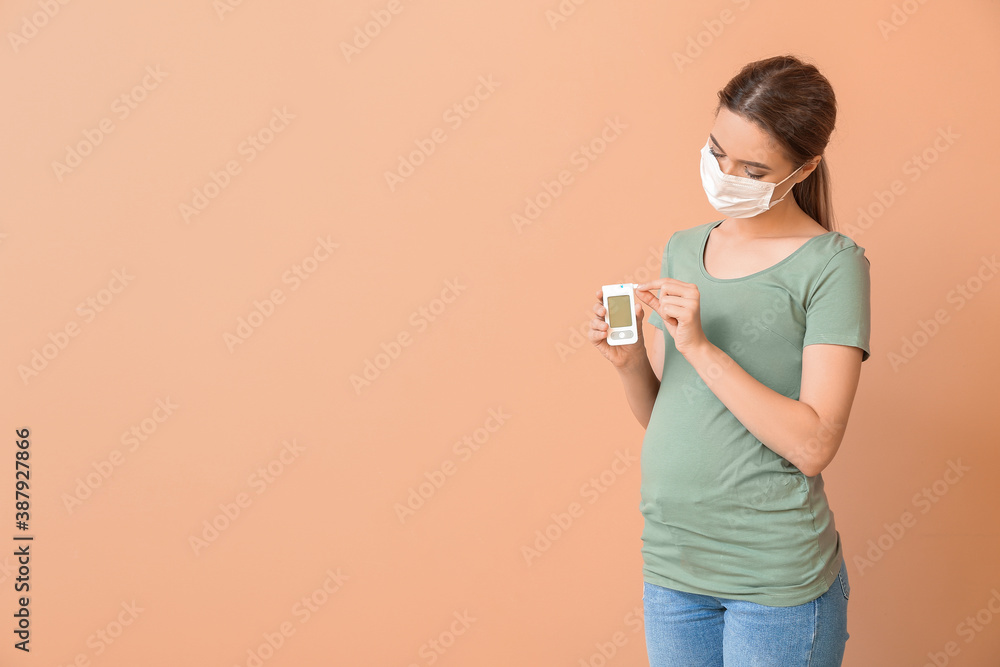Pregnant diabetic woman in medical mask and with digital glucometer on color background Pregnant diabetic woman in medical mask and with digital glucometer on color background