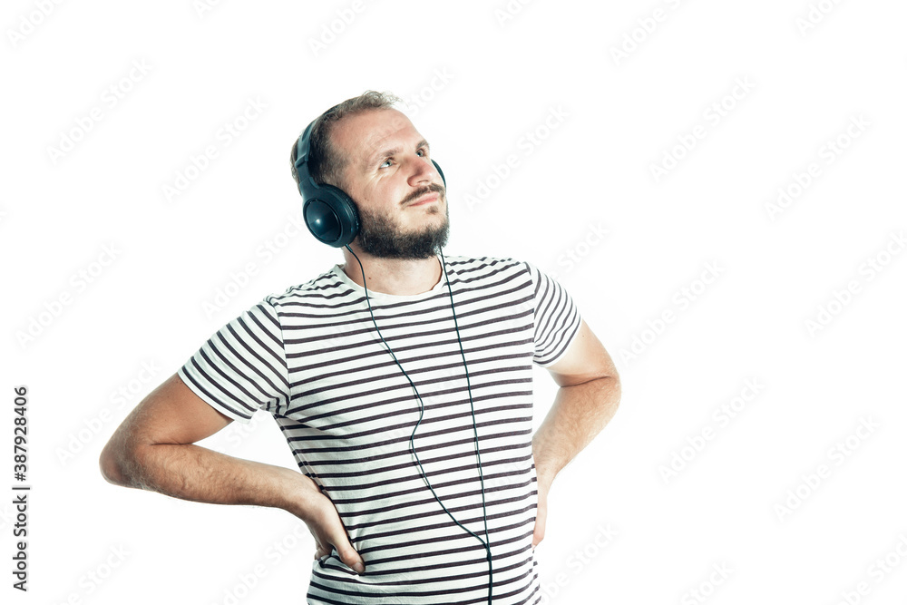 Smiling bearded happy man in a striped T-shirt listens to music with big headphones. looks to the top corner. Isolated. Smiling bearded happy man in a striped T-shirt listens to music with big headphones. looks to the top corner. Isolated.