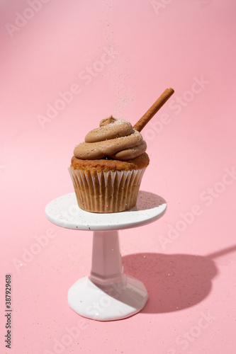 Cinnamon cupcake with frosting and s cinnamon stick on a white pedestal