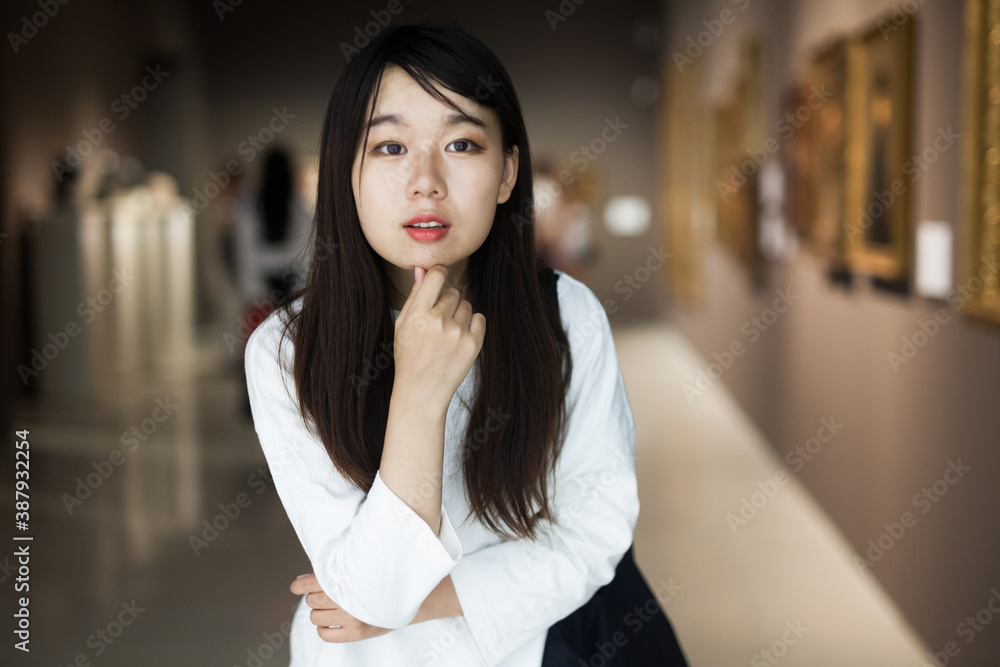 Chinese female visitor looking at artwork painting in the museum indoors
