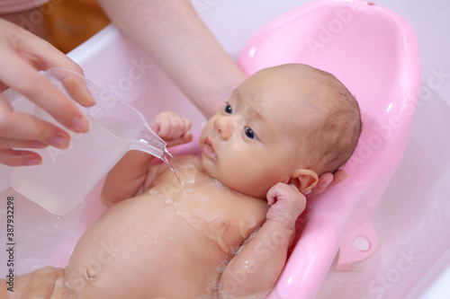 the newborn is bathed in the bathroom, the child is watered with water from a water bucket