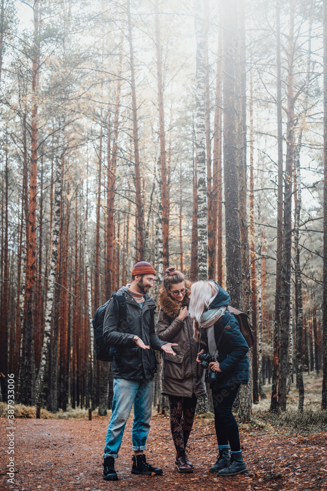 Obraz premium Bearded guy and two beautiful girls talking and getting fun exploring autumn forest.