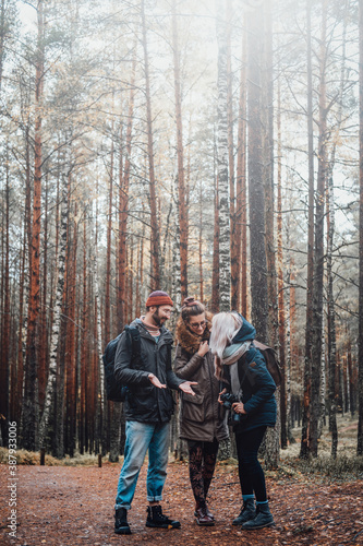 Bearded guy and two beautiful girls talking and getting fun exploring autumn forest.